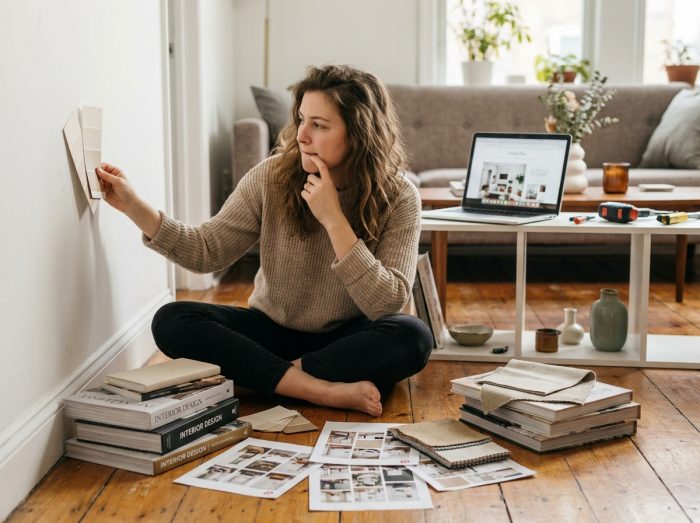 Jeune femme autodidacte en décoration intérieure comparant des échantillons de peinture entourée de livres et de planches d'inspiration